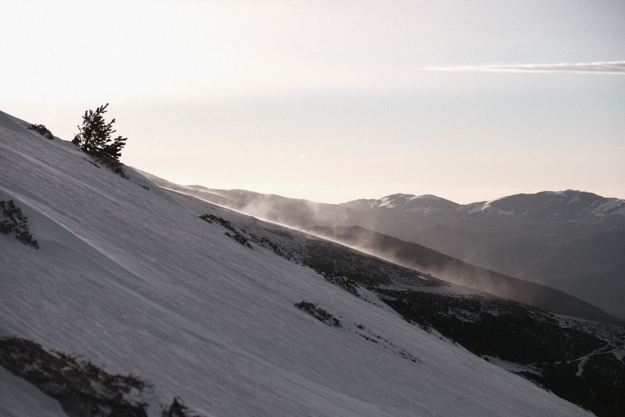 A tranquil snowy mountain slope with mist rising in the soft light of sunrise, creating a serene winter scene.