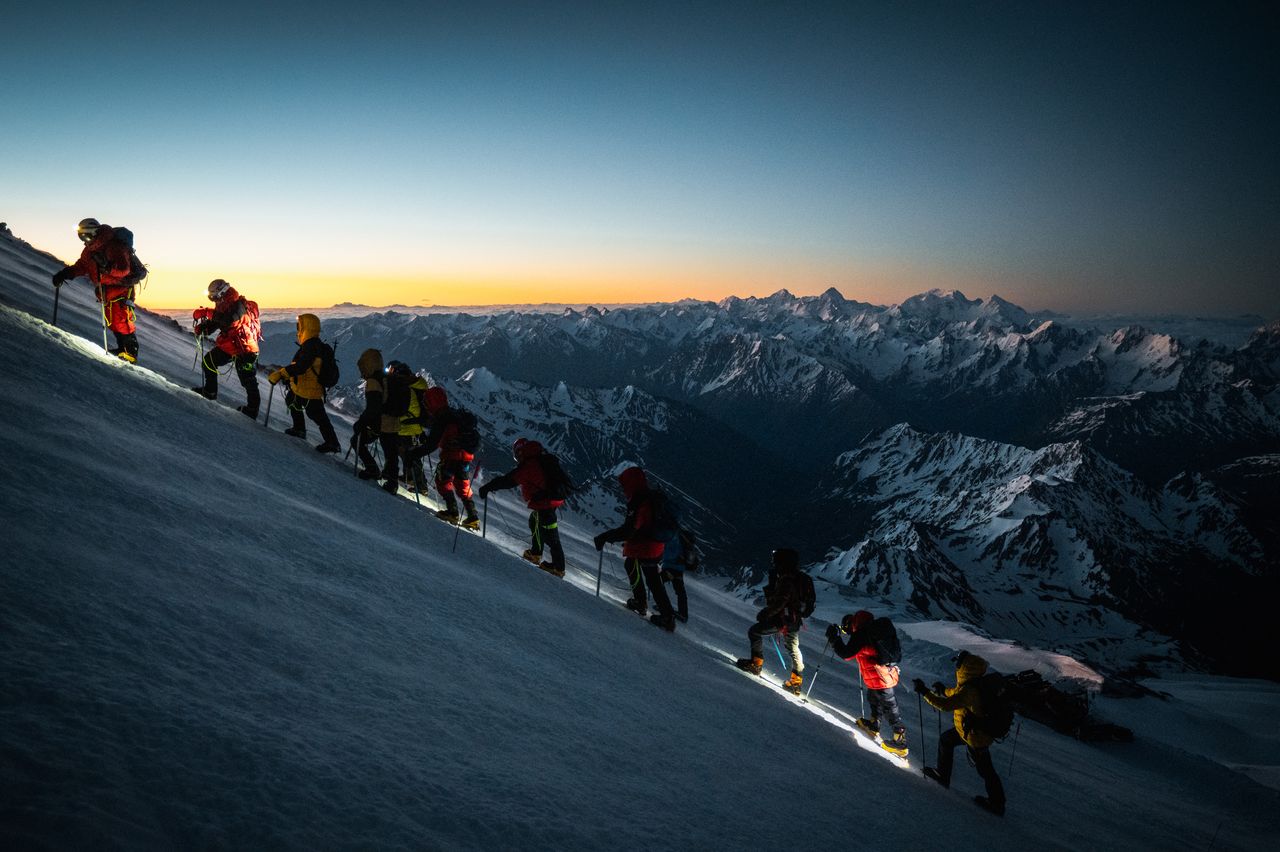 A group of climbers ascend Mount Elbrus at dawn, showcasing teamwork and adventure in the snowy Caucasus Mountains.