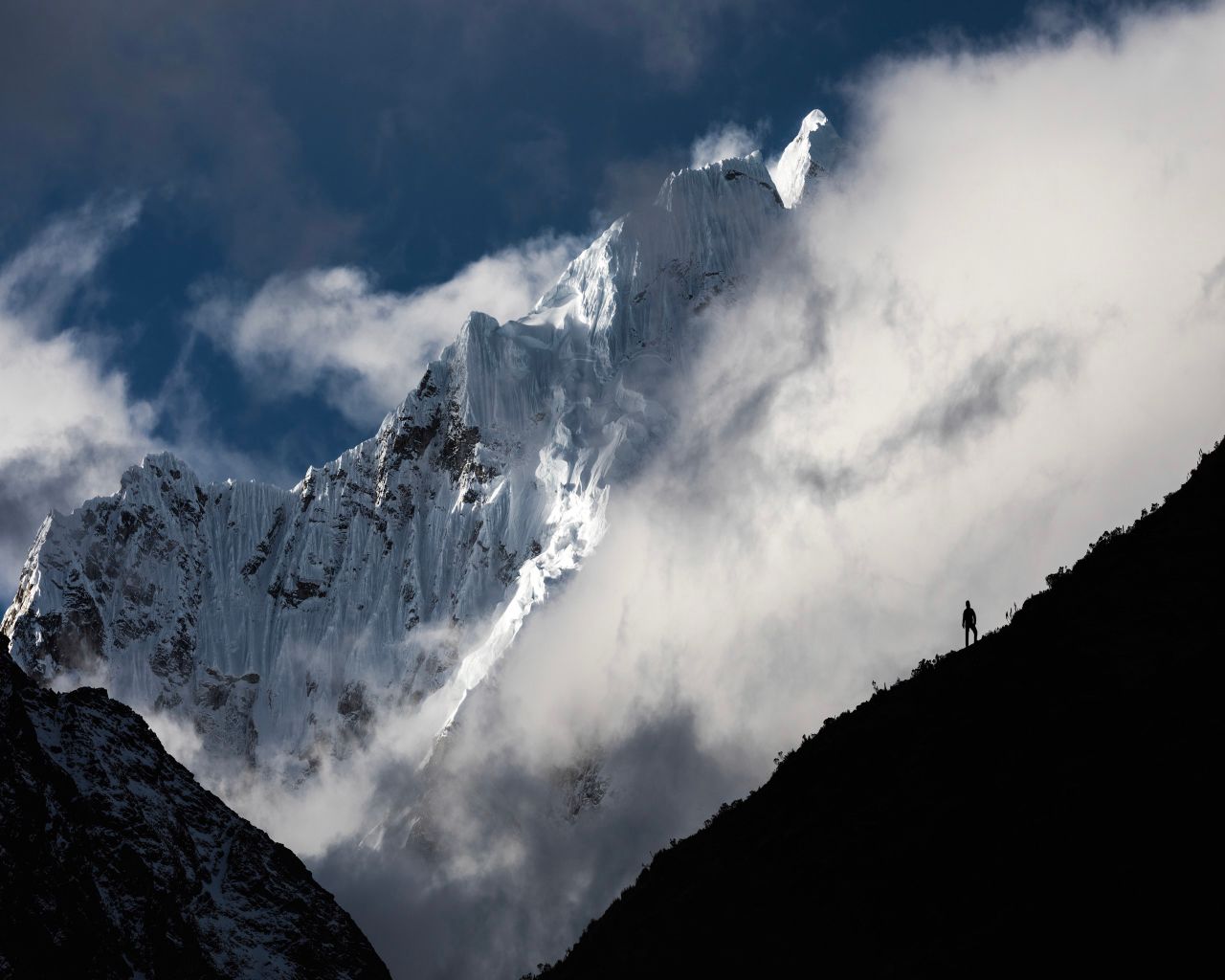 A breathtaking view of a snow-covered peak in the Andes, Peru, captured with dramatic clouds.